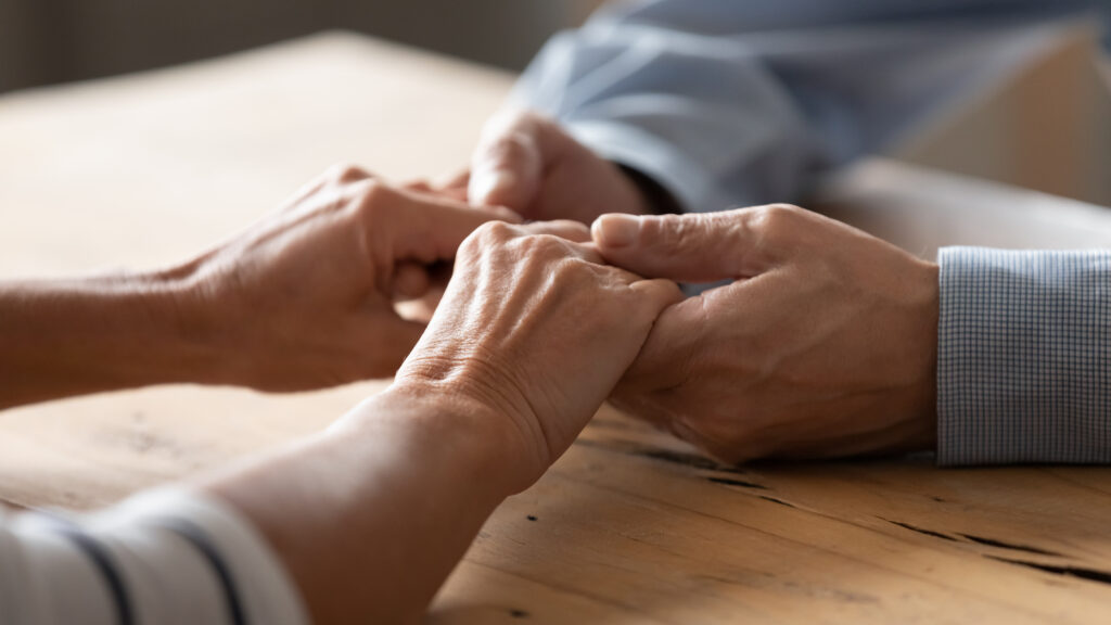 Close,Up,Older,Spouses,Holding,Hands,On,Wooden,Table,,Loving